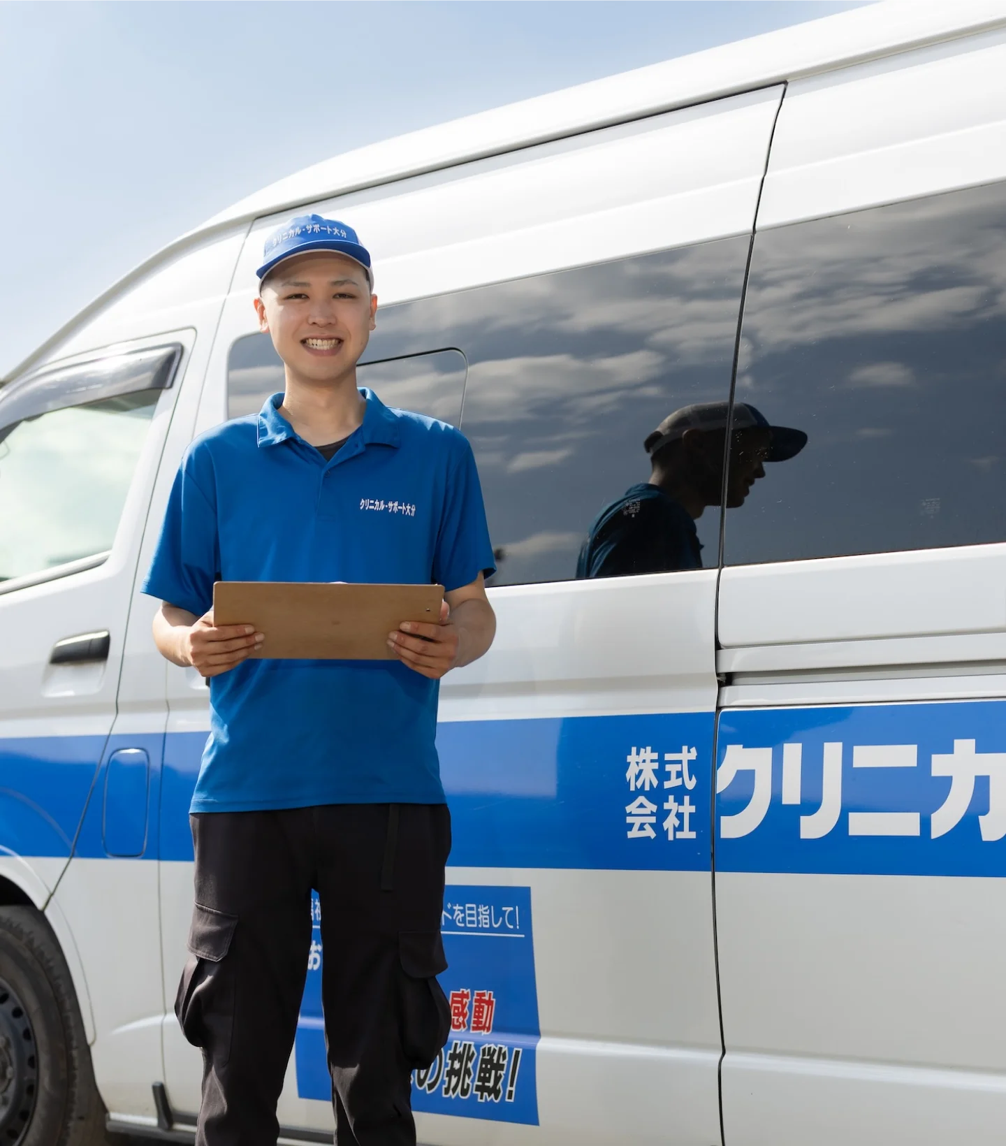 白い配送車の前で、制服を着用した従業員がクリップボードを持ちながら笑顔で立っている様子。